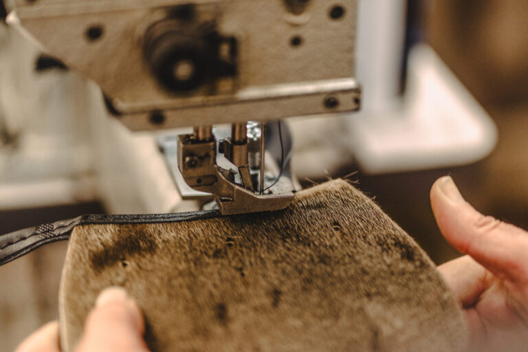 Hands stitching a hide-front sporran piece in the Glasgow workshop