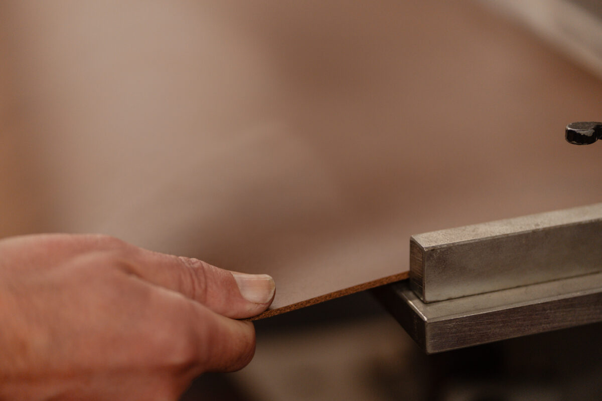 A hand guiding leather against a metal guide