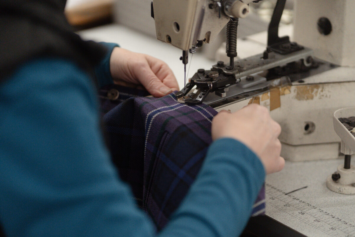 Hands stitching purple tartan at a sewing machine