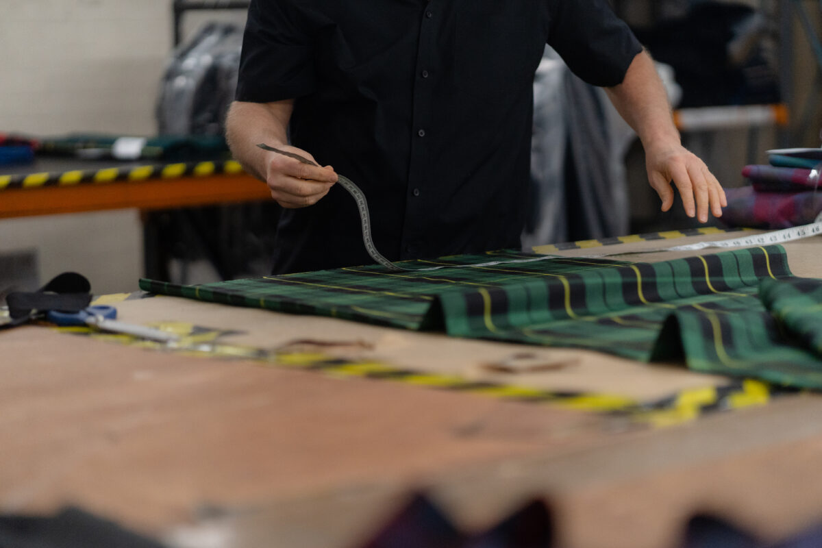 Hands measuring green tartan in the Gaelic Themes Glasgow workshop